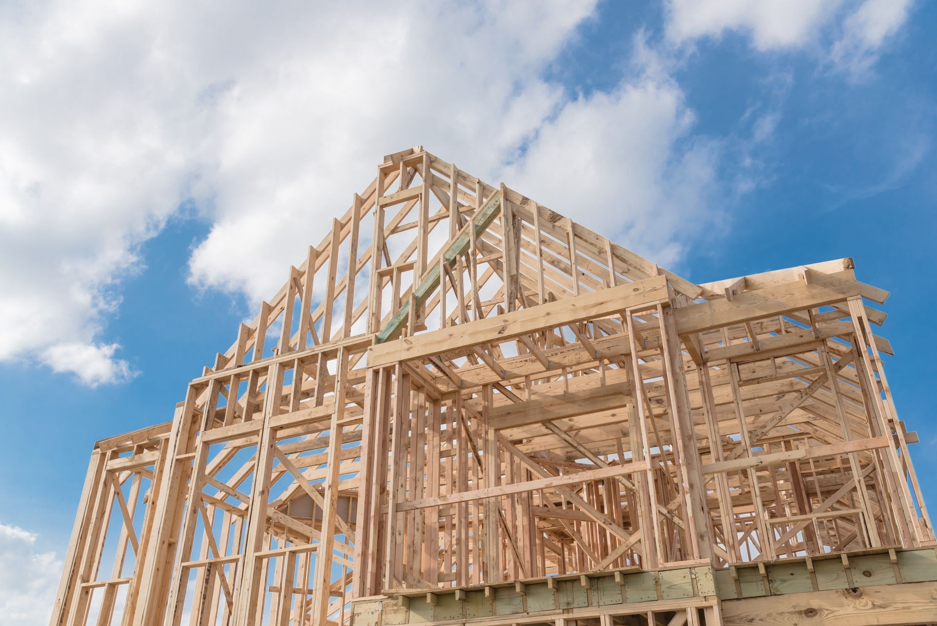 Close-up new build roof with wooden truss, post and beam framework. Gables roof on stick built home under construction and cloud blue sky. Timber frame house in South Irving, Texas, USA